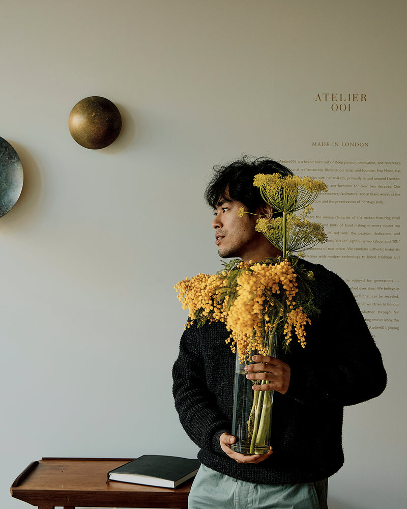 Person holding a vase of yellow flowers against a wall with decorative  elements of atelier001.