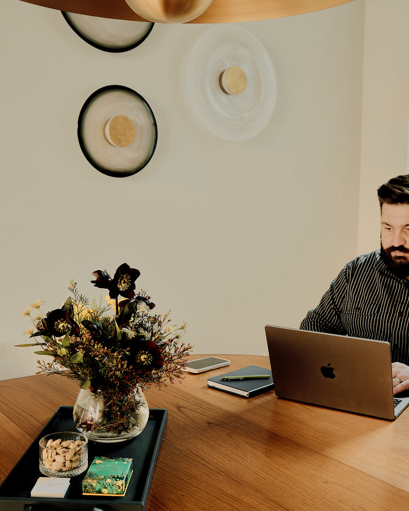 Man using a laptop at a wooden table with decorative elements and lights by Atelier001
