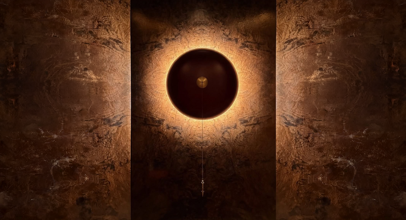 Decorative wall light fixture with a warm glow on a textured brown wall.